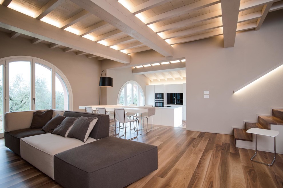 Diseño de salón con barra de bar abierto contemporáneo grande con paredes beige, suelo de madera en tonos medios, chimenea lineal, marco de chimenea de yeso y televisor colgado en la pared