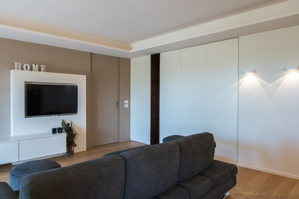 Ejemplo de salón abierto actual de tamaño medio con paredes blancas, suelo de madera clara, pared multimedia y suelo beige