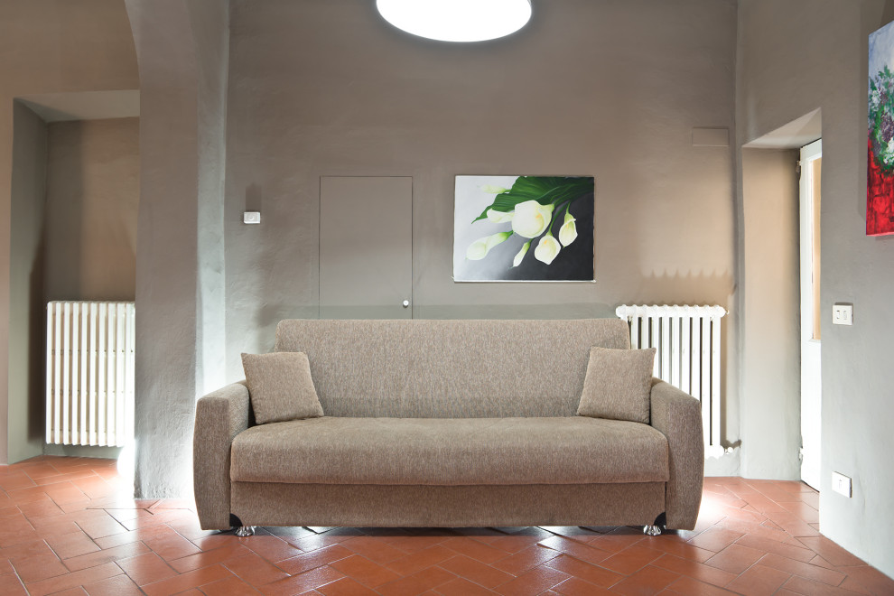 Diseño de salón abierto minimalista pequeño con paredes grises, suelo de baldosas de terracota, televisor colgado en la pared y suelo naranja