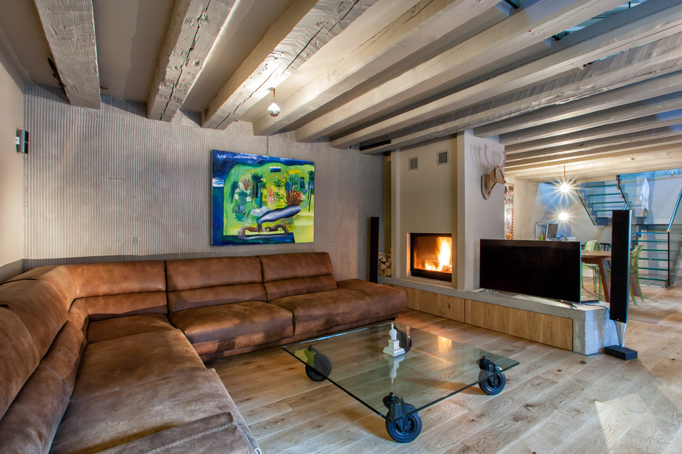 Mittelgroßes Industrial Wohnzimmer mit Tunnelkamin, verputzter Kaminumrandung, freistehendem TV und hellem Holzboden in Sonstige