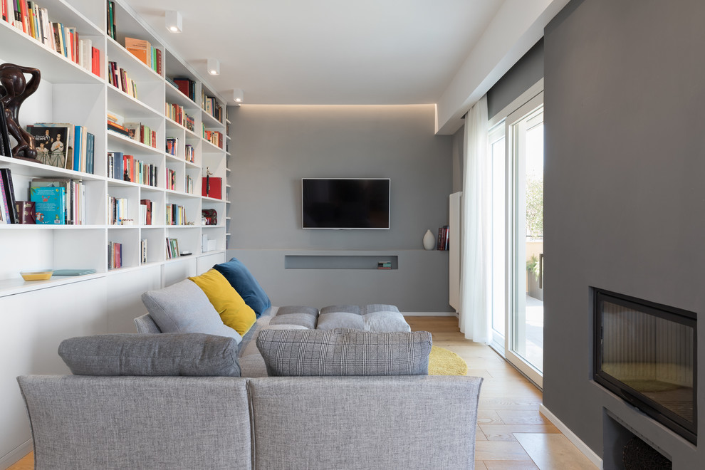 Idée de décoration pour une salle de séjour design avec une bibliothèque ou un coin lecture, un mur gris, un sol en bois brun, une cheminée standard, un téléviseur fixé au mur et un sol marron.