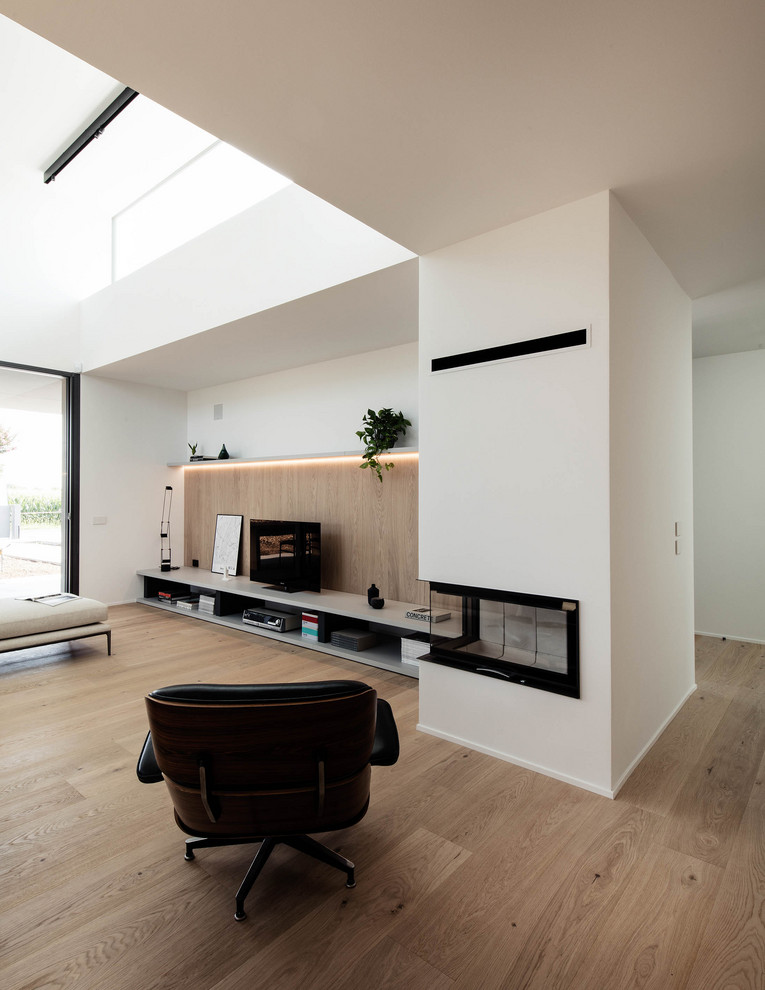 Immagine di un grande soggiorno minimalista aperto con pareti bianche, parquet chiaro, camino ad angolo e TV autoportante