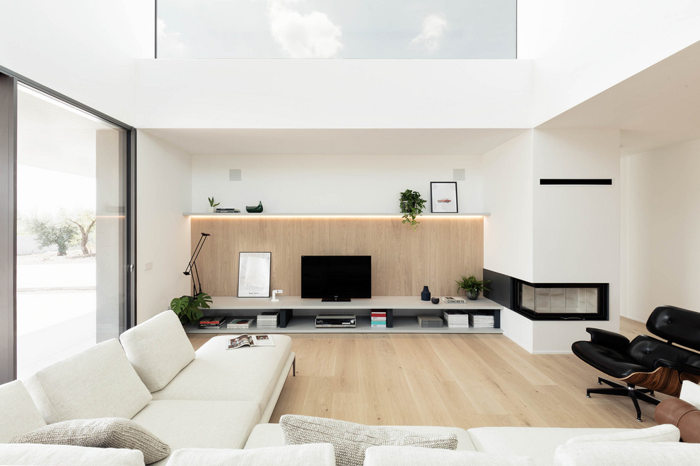 Esempio di un grande soggiorno minimalista aperto con pareti bianche, parquet chiaro, camino ad angolo e TV autoportante