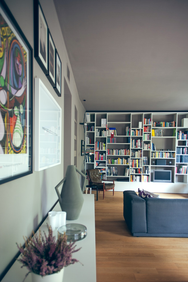 Ejemplo de sala de estar con biblioteca abierta escandinava grande con paredes grises, suelo de madera clara y pared multimedia