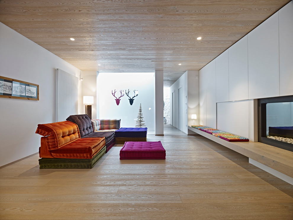 Foto de salón abierto actual grande con paredes blancas, suelo de madera clara, chimenea lineal y marco de chimenea de yeso