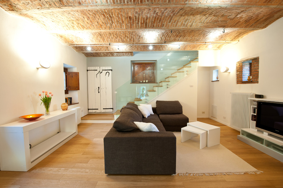 Modelo de sala de estar con biblioteca cerrada actual de tamaño medio con paredes blancas, suelo de madera clara, marco de chimenea de yeso y pared multimedia