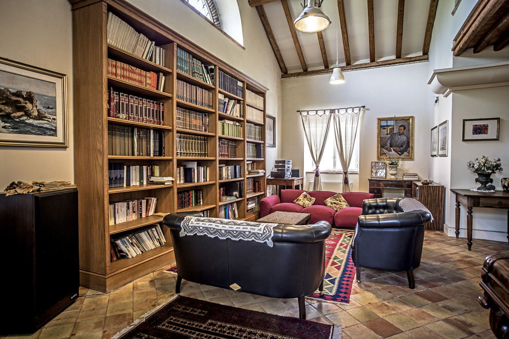 Aménagement d'une grande salle de séjour campagne ouverte avec une bibliothèque ou un coin lecture, un mur blanc et tomettes au sol.