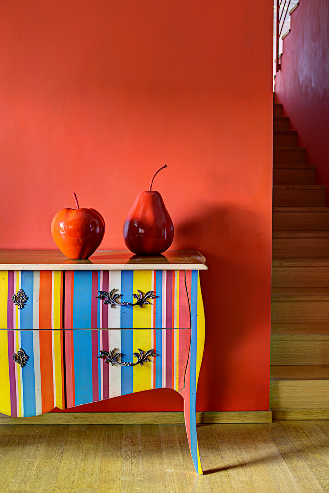 Cette image montre une salle de séjour de taille moyenne et ouverte avec un mur rouge, un sol en bois brun, aucune cheminée et un sol marron.