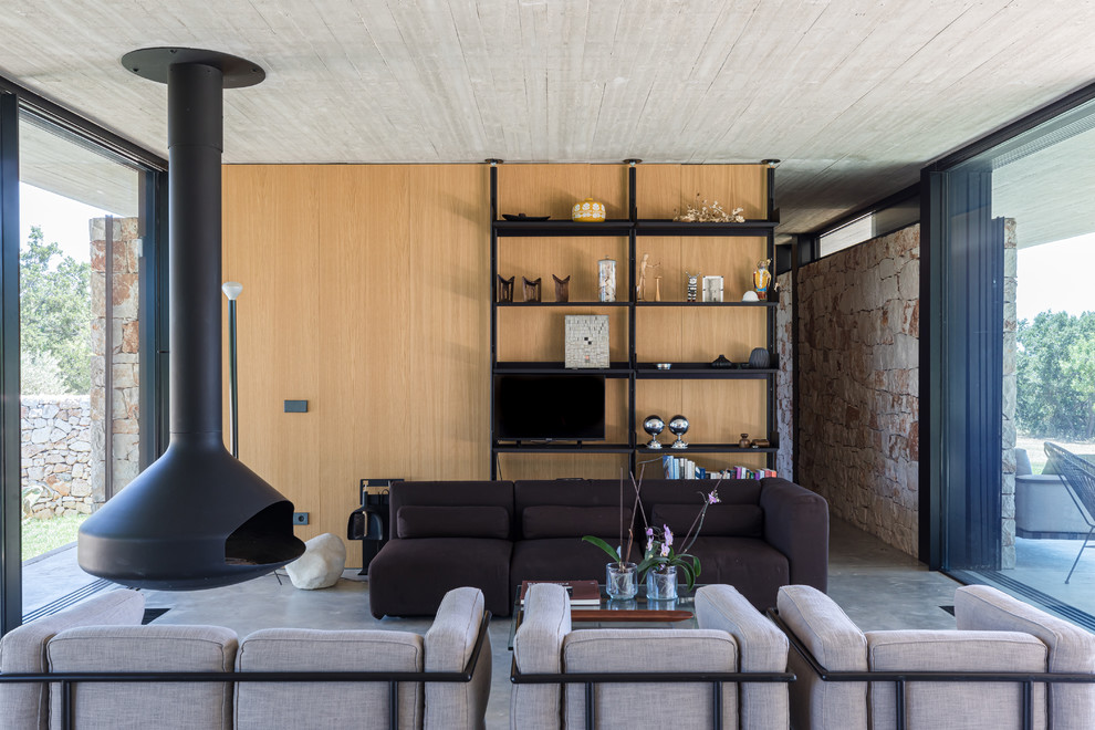 Inspiration pour un salon design avec un mur marron, sol en béton ciré, cheminée suspendue, un téléviseur indépendant, un sol gris et canapé noir.