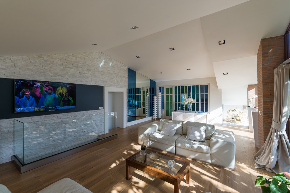 Diseño de salón abierto actual grande con paredes blancas, suelo de baldosas de porcelana, televisor colgado en la pared y suelo marrón
