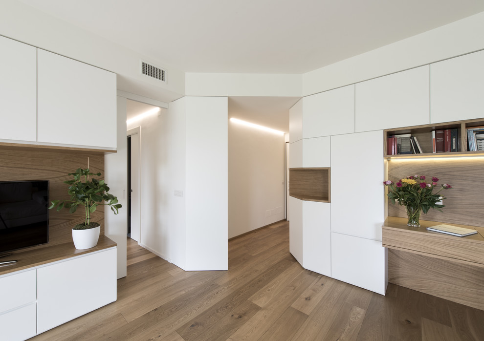На фото: большая открытая гостиная комната в стиле модернизм с с книжными шкафами и полками, белыми стенами, светлым паркетным полом, телевизором на стене и бежевым полом