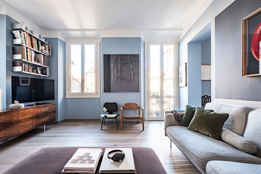 Kleine Nordische Bibliothek im Loft-Stil mit blauer Wandfarbe, hellem Holzboden, freistehendem TV und beigem Boden in Mailand