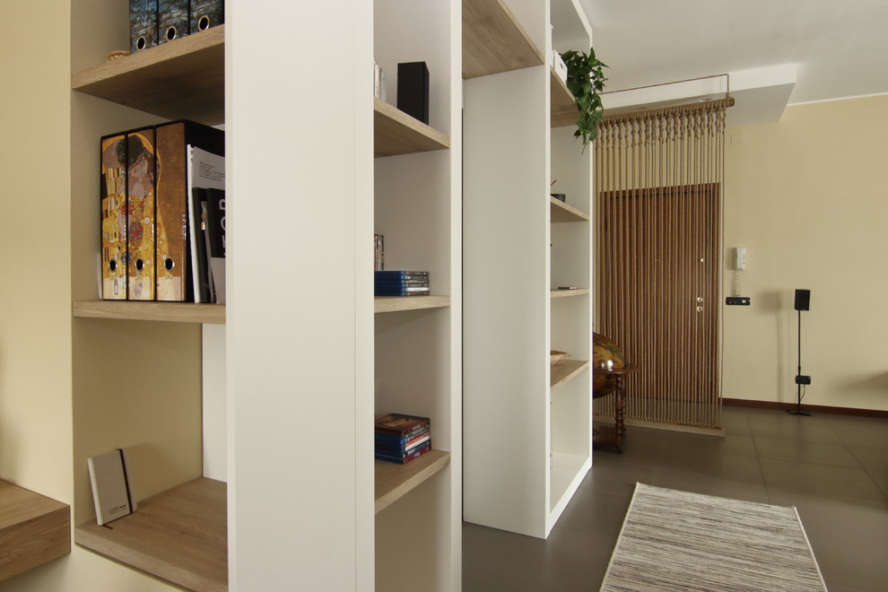 Modelo de biblioteca en casa abierta asiática de tamaño medio con paredes beige, suelo de baldosas de cerámica, televisor colgado en la pared y suelo marrón
