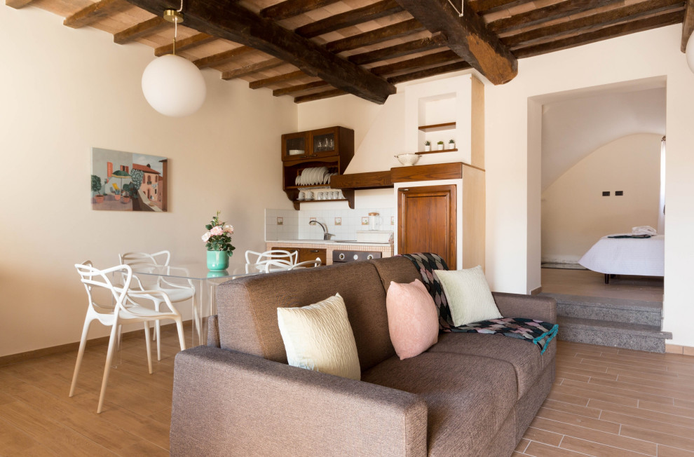 Пример оригинального дизайна: открытая гостиная комната среднего размера в средиземноморском стиле с белыми стенами, полом из керамогранита, стандартным камином, фасадом камина из камня, коричневым полом и балками на потолке
