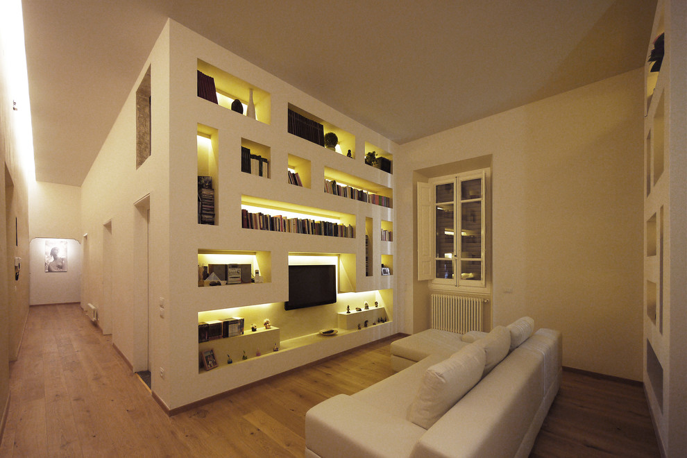 На фото: большая открытая гостиная комната в стиле модернизм с с книжными шкафами и полками, белыми стенами, светлым паркетным полом, телевизором на стене и коричневым полом без камина с