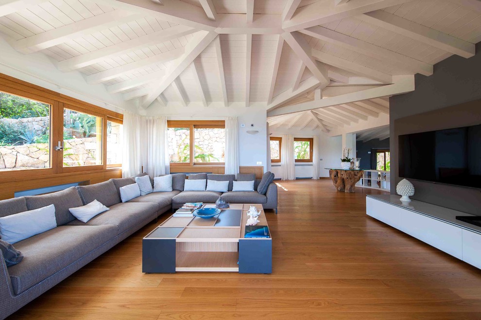 Imagen de sala de estar abierta contemporánea con paredes blancas, suelo de madera en tonos medios y televisor colgado en la pared
