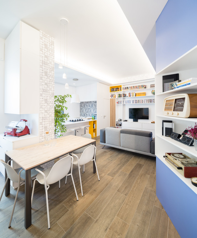 Пример оригинального дизайна: маленькая открытая гостиная комната в современном стиле с с книжными шкафами и полками, синими стенами, полом из керамогранита, телевизором на стене и коричневым полом для на участке и в саду
