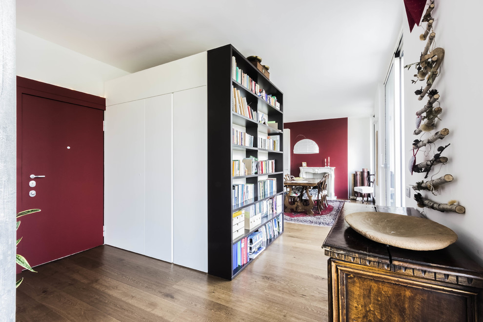 Kleine, Offene Moderne Bibliothek mit roter Wandfarbe, braunem Holzboden, Kamin, Kaminumrandung aus Stein, TV-Wand und braunem Boden in Mailand