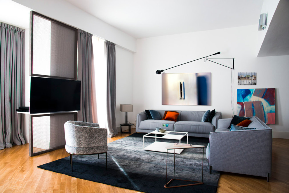 На фото: гостиная комната в современном стиле с белыми стенами, паркетным полом среднего тона, телевизором на стене и коричневым полом