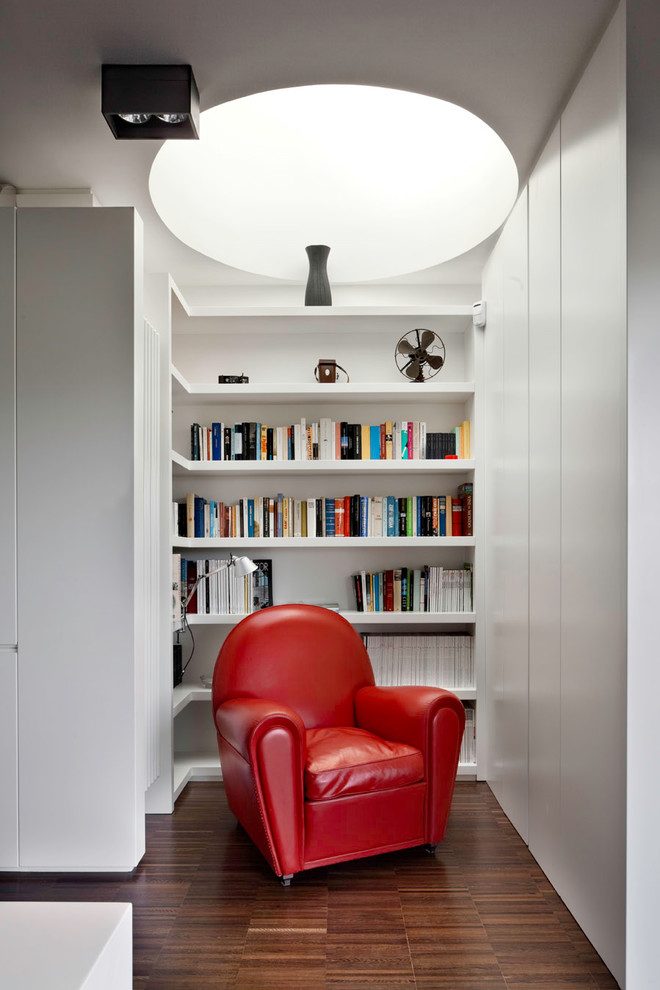 Cette image montre une petite salle de séjour design avec une bibliothèque ou un coin lecture, un mur blanc, aucune cheminée et parquet foncé.