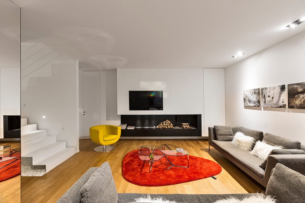 Пример оригинального дизайна: большая открытая гостиная комната в современном стиле с белыми стенами, светлым паркетным полом, горизонтальным камином, телевизором на стене и ковром на полу