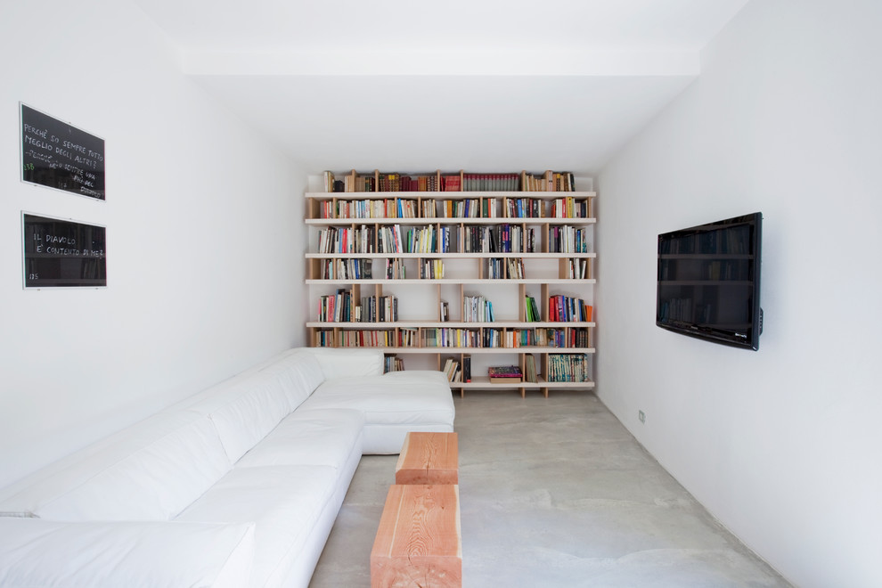 Imagen de sala de estar con biblioteca minimalista con paredes blancas, suelo de cemento y televisor colgado en la pared