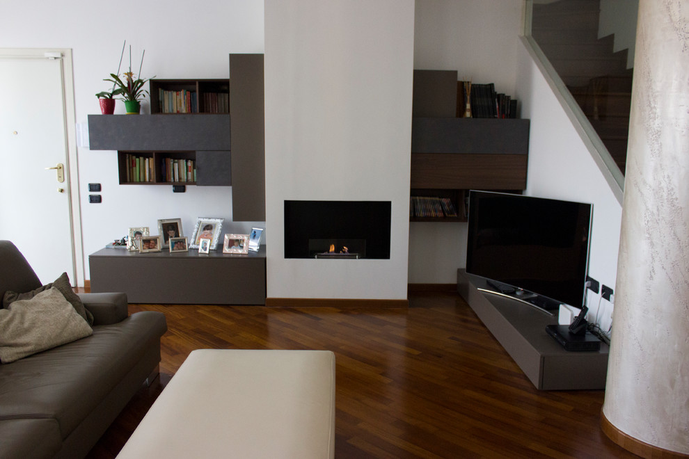 Ejemplo de sala de estar con biblioteca abierta minimalista grande con paredes blancas, suelo de madera oscura, chimenea lineal, marco de chimenea de yeso, pared multimedia y suelo marrón