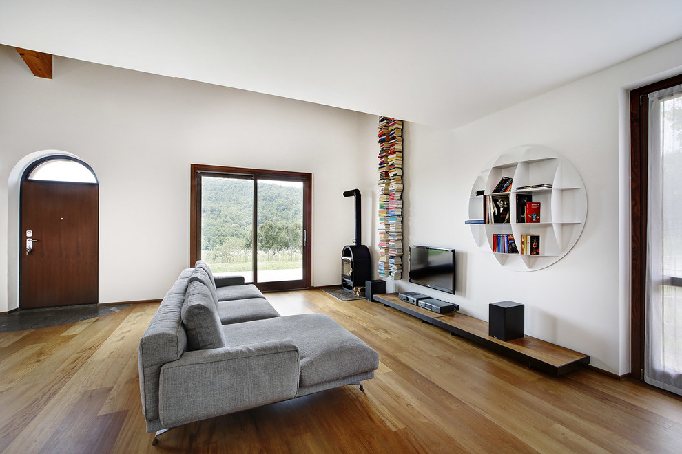 Exempel på ett modernt allrum, med vita väggar, mellanmörkt trägolv, en väggmonterad TV och ett bibliotek