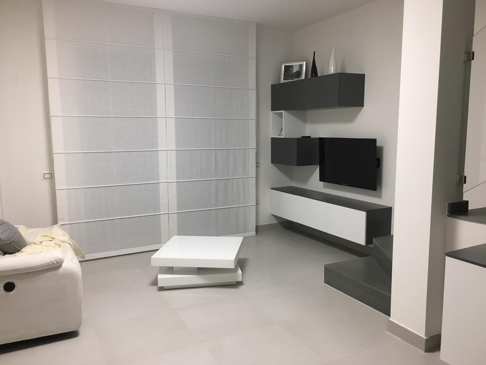 Стильный дизайн: открытая гостиная комната среднего размера в стиле модернизм с белыми стенами, отдельно стоящим телевизором и белым полом - последний тренд