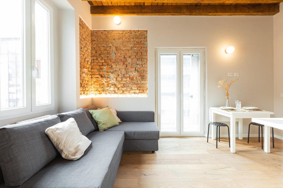 Imagen de salón abierto nórdico pequeño sin chimenea con paredes blancas, suelo de madera clara, vigas vistas y ladrillo