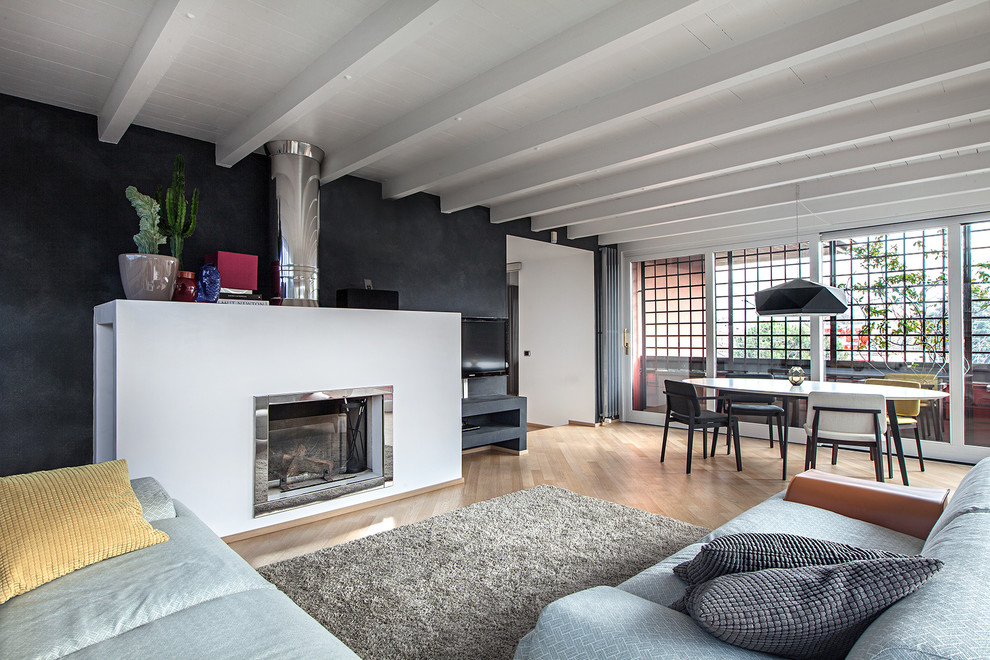 This is an example of a large contemporary open plan living room in Milan with black walls, light hardwood flooring, a ribbon fireplace, a wall mounted tv and a metal fireplace surround.