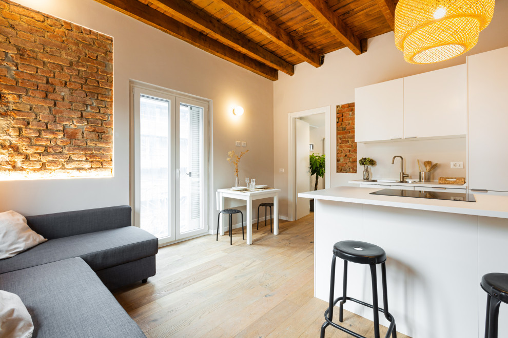 Kleines, Offenes Nordisches Wohnzimmer ohne Kamin mit weißer Wandfarbe, hellem Holzboden, freigelegten Dachbalken und Ziegelwänden in Mailand