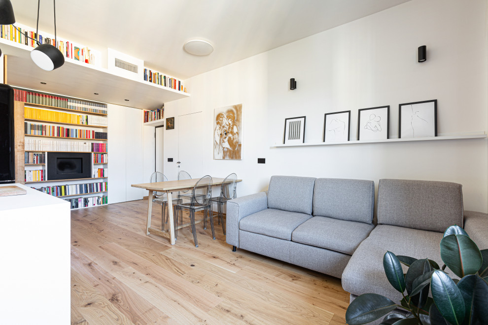 Ejemplo de sala de estar con biblioteca abierta escandinava grande con paredes blancas, suelo de madera clara, chimeneas suspendidas, marco de chimenea de metal, televisor colgado en la pared y bandeja