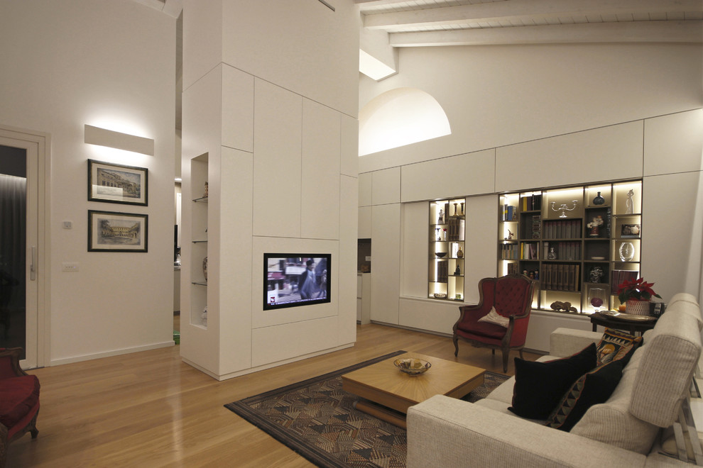 This is an example of a large open plan living room in Milan with a reading nook, white walls, medium hardwood flooring, a wall mounted tv and brown floors.