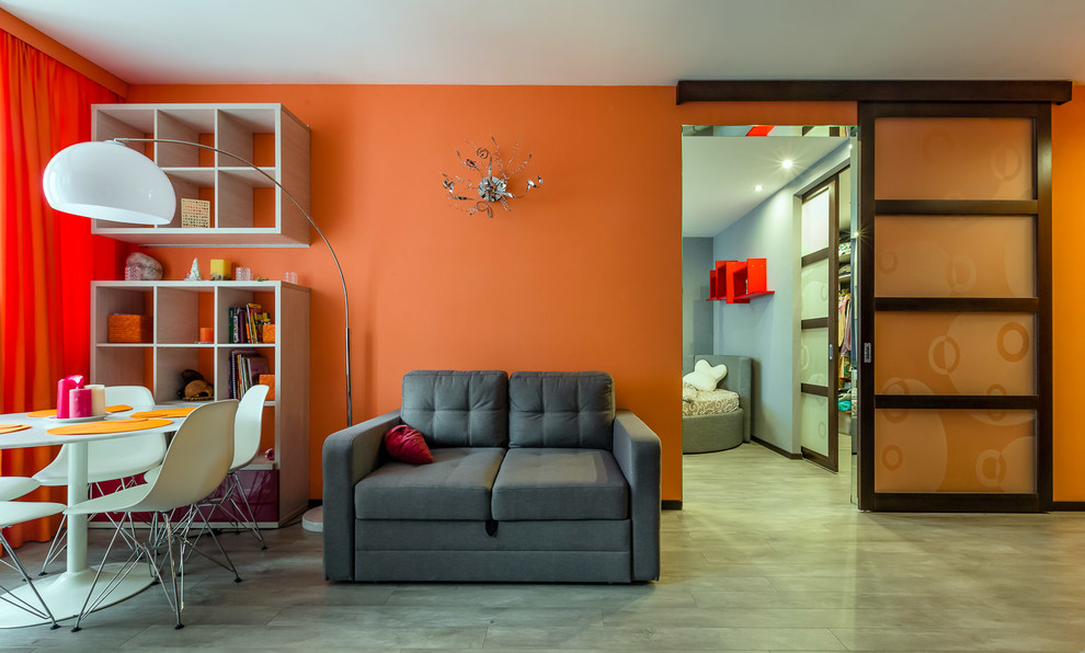 Источник вдохновения для домашнего уюта: открытая гостиная комната среднего размера в стиле модернизм с с книжными шкафами и полками, оранжевыми стенами, полом из ламината, телевизором на стене и серым полом