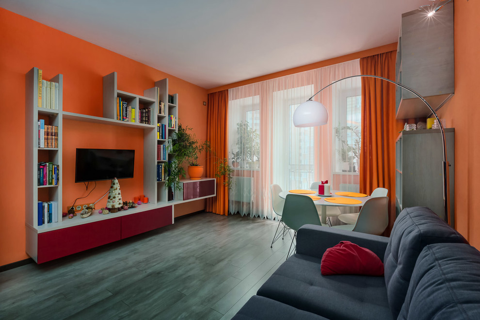 Идея дизайна: открытая гостиная комната среднего размера в стиле модернизм с с книжными шкафами и полками, оранжевыми стенами, полом из ламината, телевизором на стене и серым полом