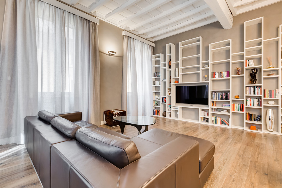Diseño de sala de estar con biblioteca abierta actual de tamaño medio con paredes beige, suelo de madera en tonos medios, televisor colgado en la pared y suelo marrón
