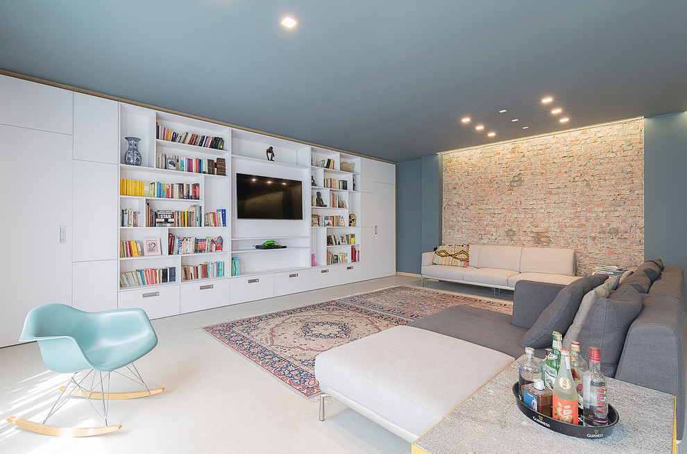 На фото: большая гостиная комната в современном стиле с бетонным полом, серым полом, с книжными шкафами и полками, синими стенами, мультимедийным центром и ковром на полу без камина