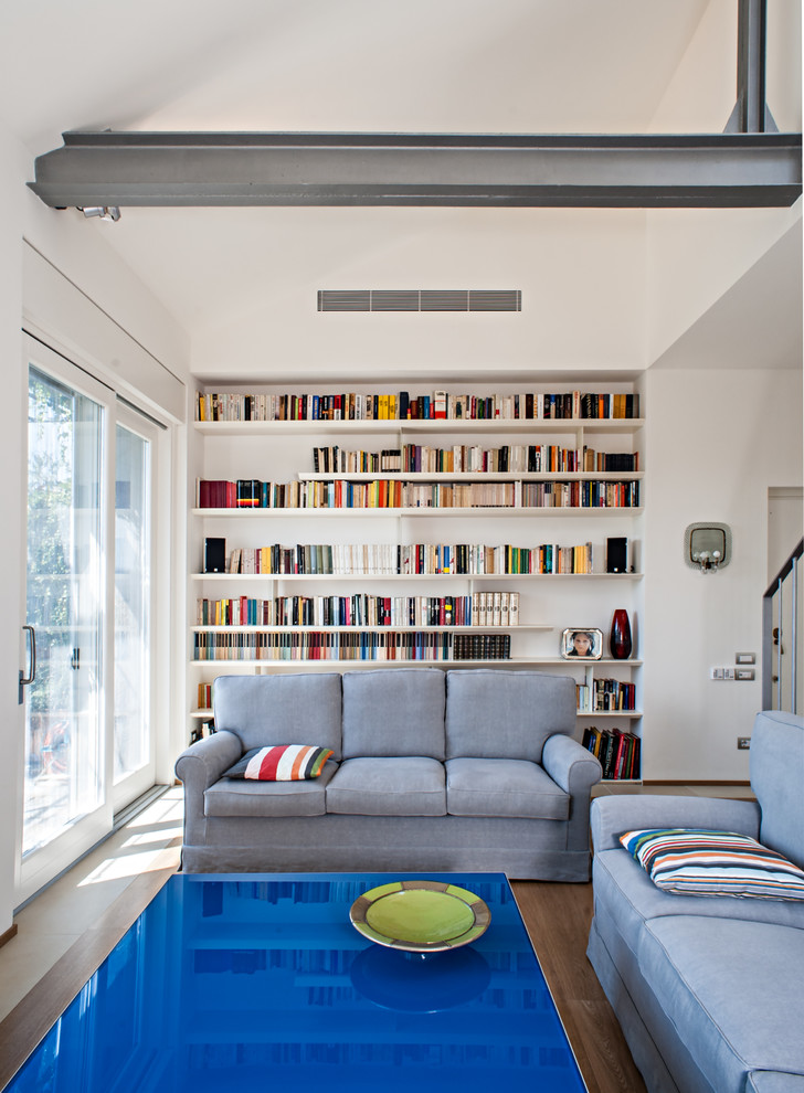 Cette image montre une grande salle de séjour design ouverte avec une bibliothèque ou un coin lecture, un mur blanc et un sol en bois brun.