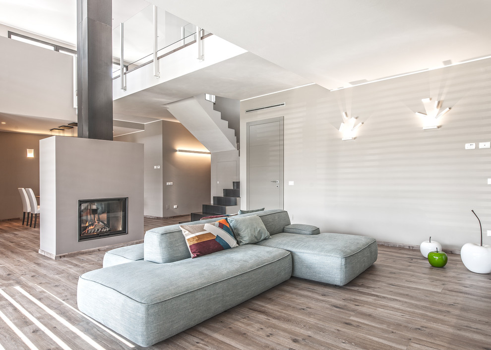 Diseño de salón para visitas abierto contemporáneo con paredes grises, suelo de madera clara, chimenea de doble cara y marco de chimenea de yeso