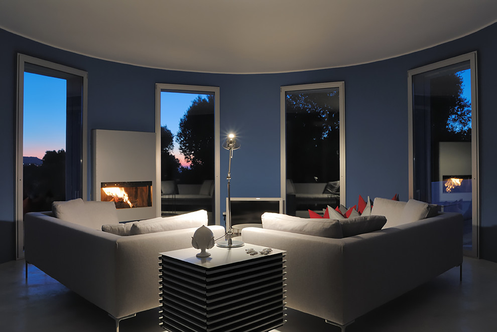 На фото: открытая гостиная комната в стиле модернизм с синими стенами, бетонным полом и фасадом камина из металла с