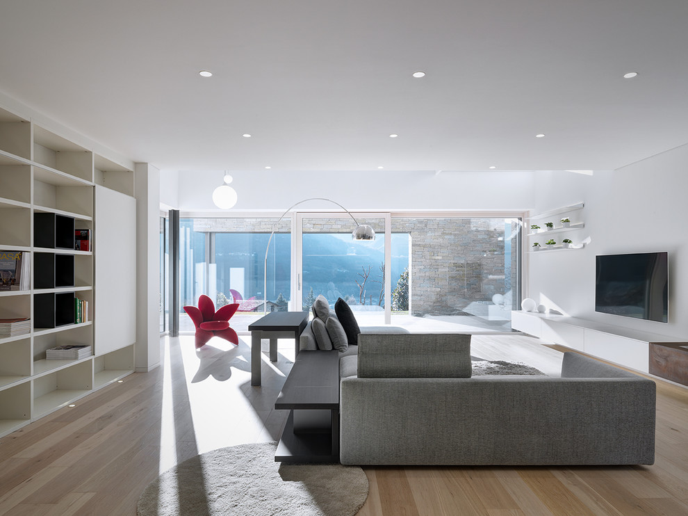 Esempio di un grande soggiorno moderno aperto con pareti bianche, pavimento in legno massello medio e TV a parete
