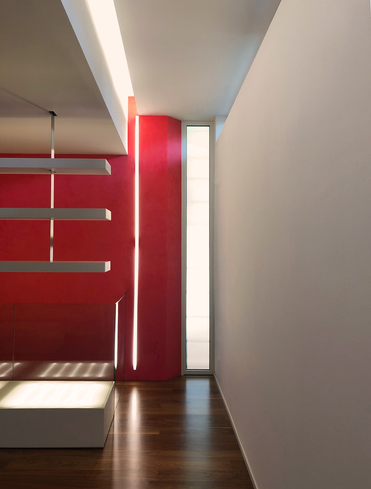 Идея дизайна: большая открытая гостиная комната в современном стиле с с книжными шкафами и полками, красными стенами, деревянным полом, горизонтальным камином, фасадом камина из металла, отдельно стоящим телевизором и коричневым полом