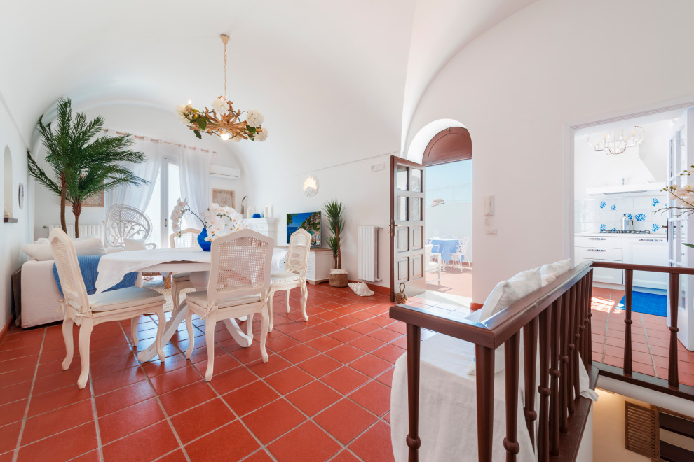 Immagine di una grande sala da pranzo mediterranea con pareti bianche, camino classico, cornice del camino in intonaco, pavimento marrone e soffitto a volta