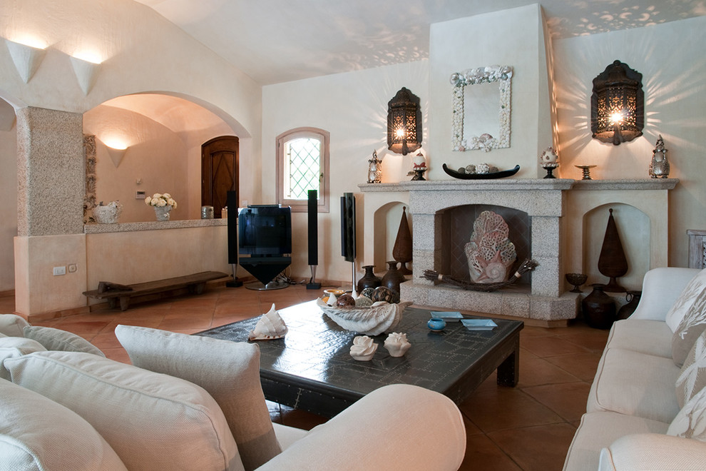 Modelo de salón abierto mediterráneo grande con paredes blancas, suelo de baldosas de terracota, todas las chimeneas, marco de chimenea de piedra, televisor en una esquina y suelo rosa