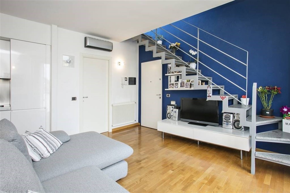 Medium sized modern open plan living room in Milan with blue walls, light hardwood flooring and a freestanding tv.