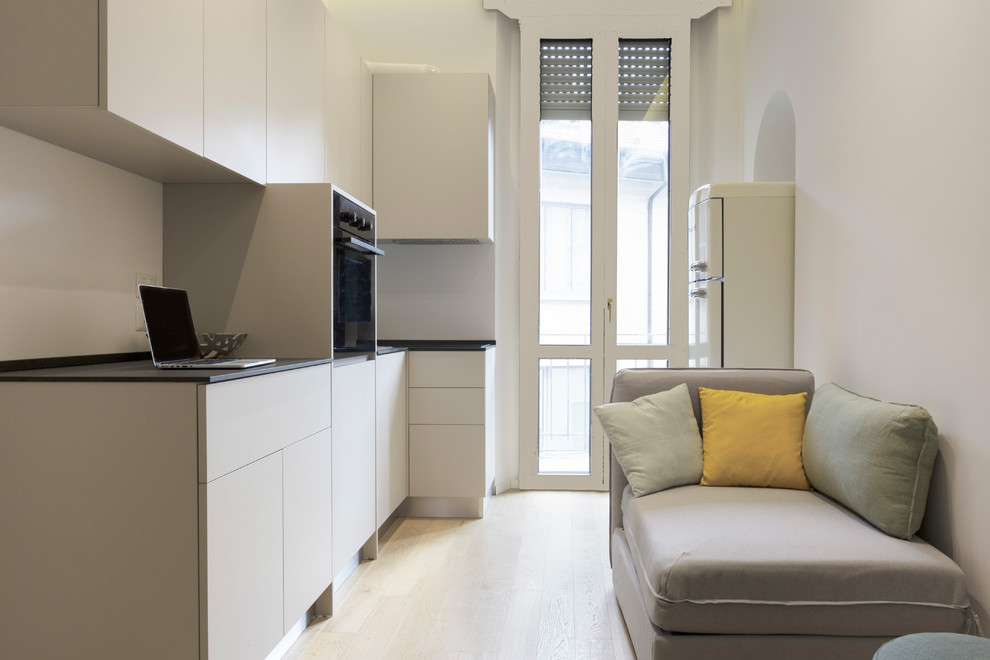 На фото: маленькая изолированная гостиная комната в современном стиле с белыми стенами, светлым паркетным полом и телевизором на стене без камина для на участке и в саду