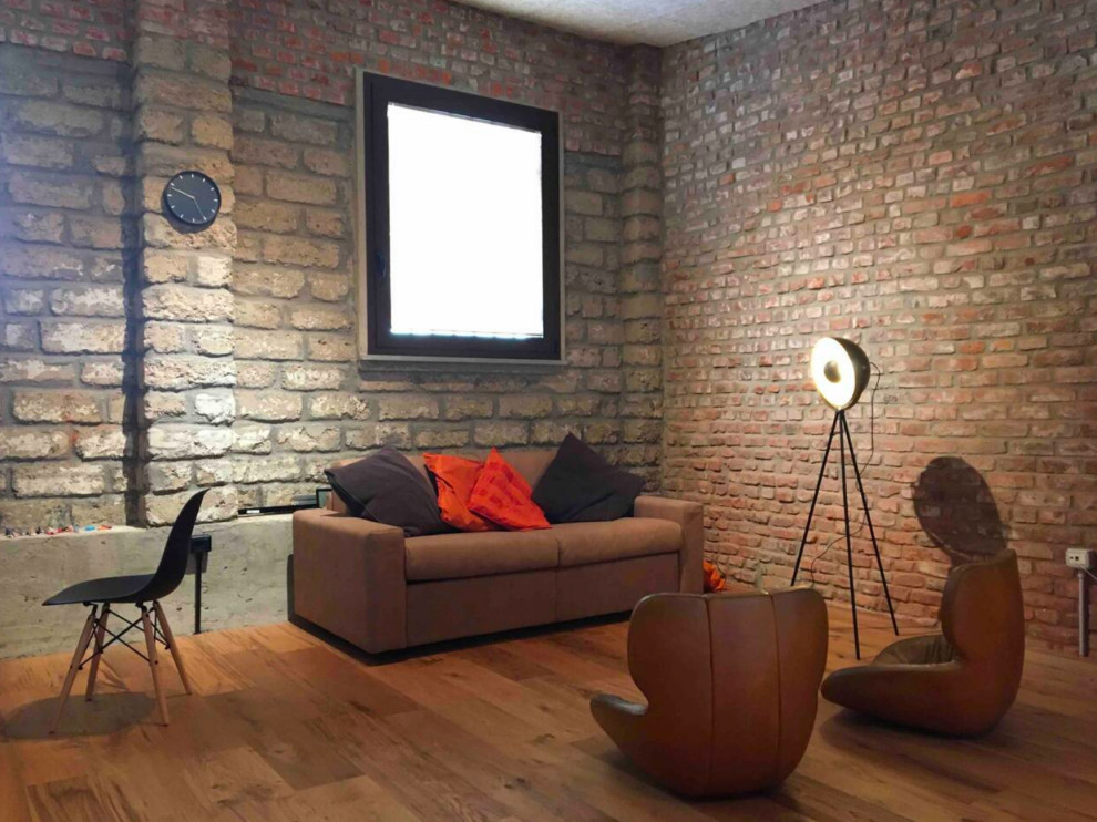 Cette photo montre un petit salon mansardé ou avec mezzanine industriel avec une salle de réception, un mur multicolore, un sol en bois brun et un téléviseur dissimulé.