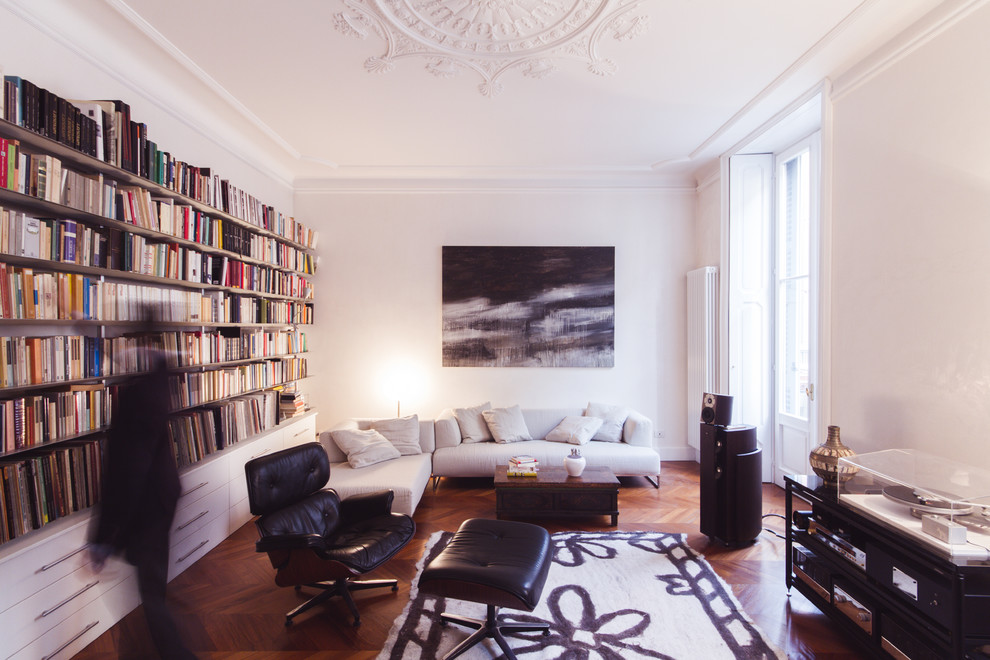 Cette image montre un salon design avec une bibliothèque ou un coin lecture, un mur blanc et parquet clair.