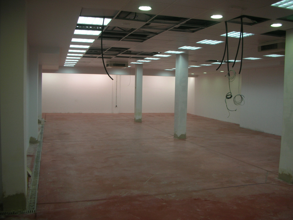 Foto på en mycket stor funkis källare utan ingång, med vita väggar, betonggolv och rött golv